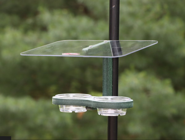 Green bird feeder is pole mounted with two clips. Holds two clear removable plastic cups. Large clear roof. 