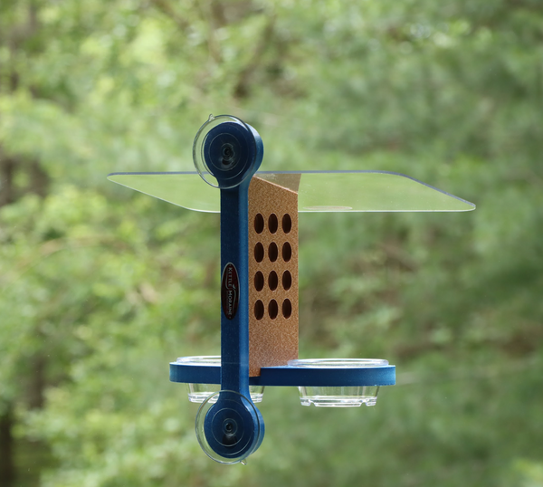 Recycled plastic window mount feeder with 2 suction cups and blue mounting bracket. Has 12 holes on both sides of brown body, a clear acrylic roof, and blue base holds 2 clear cups. 